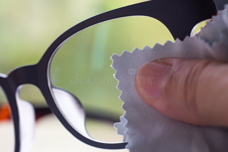 Woman right hand cleaning grey shortsighted or nearsighted eyeglasses by grey microfibre cleaning cloths, Bokeh green bg.