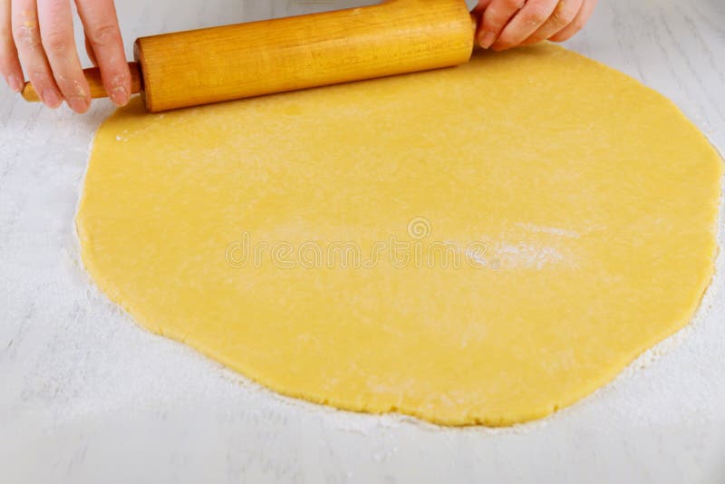 Woman rolling dough with pin for making cookies on white table