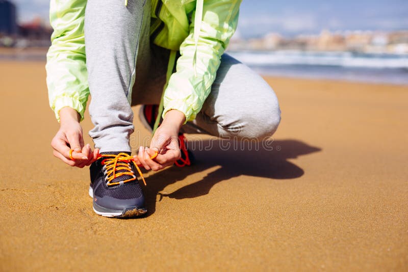 Fitness woman getting ready for running challenge at city beach in Gijon, Asturias, Spain. Female runner lacing sport shoes before training. Fitness woman getting ready for running challenge at city beach in Gijon, Asturias, Spain. Female runner lacing sport shoes before training.