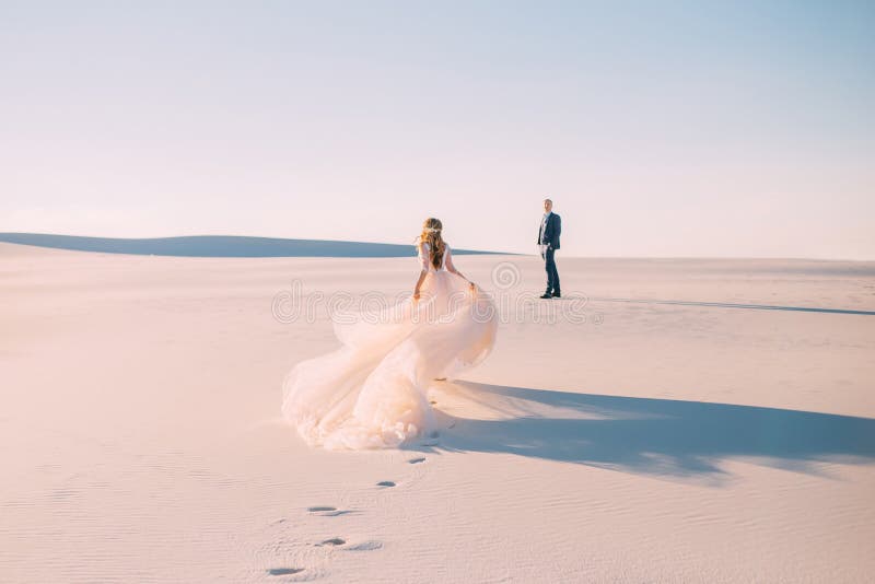 A women runs to meet a man. Dress with a very long hairpin that flies in the wind. Photo from the back without a face. Background desert at sunset. Fine art photo. A women runs to meet a man. Dress with a very long hairpin that flies in the wind. Photo from the back without a face. Background desert at sunset. Fine art photo.