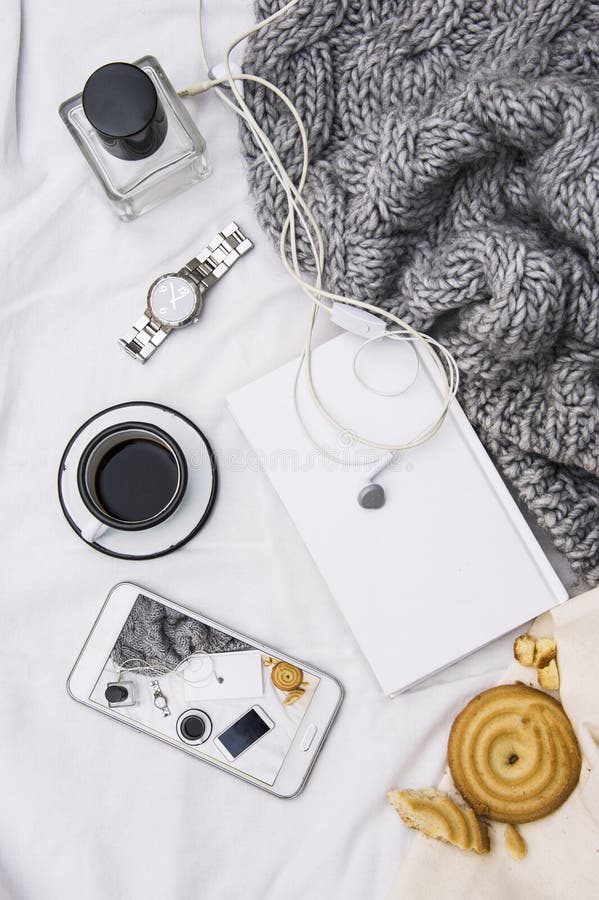 Woman`s bed top view on a lazy sunday morning in cold weather . Lifestyle with mobile phone, book, cakes