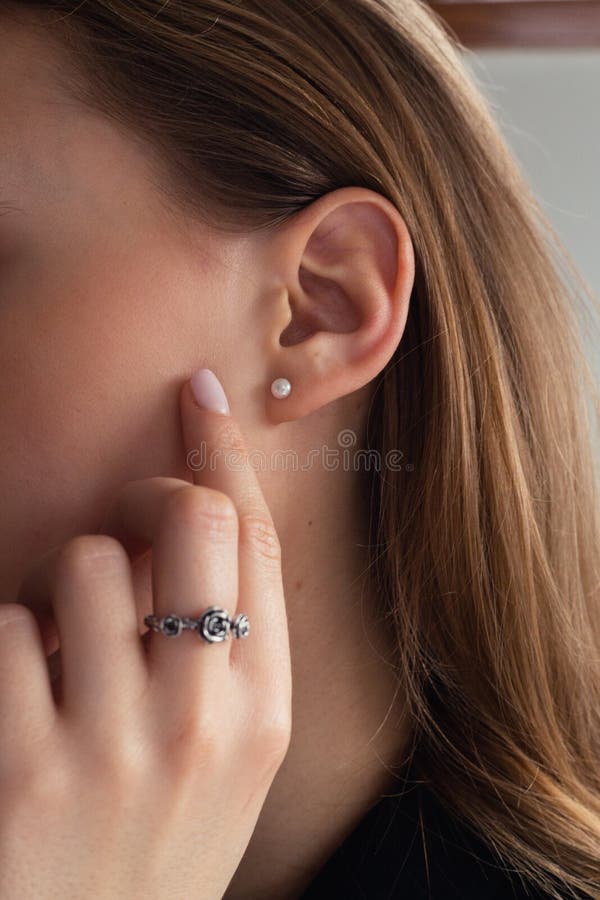 Woman`s ear close-up. Pearl earring, natural blonde woman touching her face