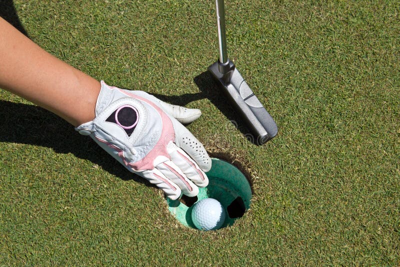 Woman's gloved hand, putter and golf ball in the cup