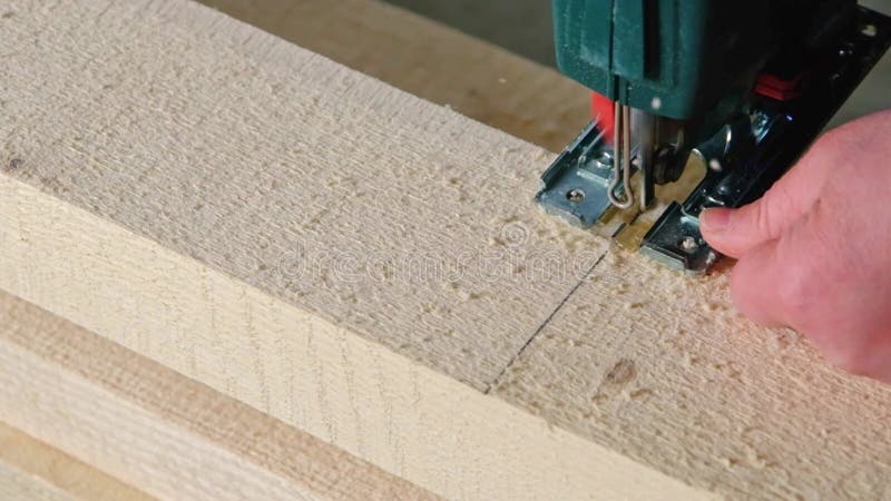 Woman`s hand cuts a board with an electric jigsaw in close-up. Carpentry on wood with a tool, sawdust flies, the saw cuts in a str