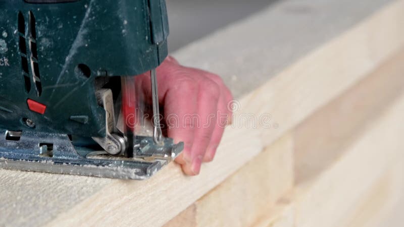 Woman`s hand cuts a board with an electric jigsaw in close-up. Carpentry on wood with a tool, sawdust flies, the saw cuts in a str