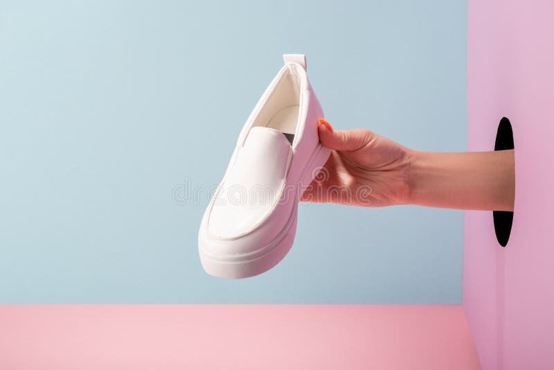 Woman`s hand holding a white loafer through a hole in the wall