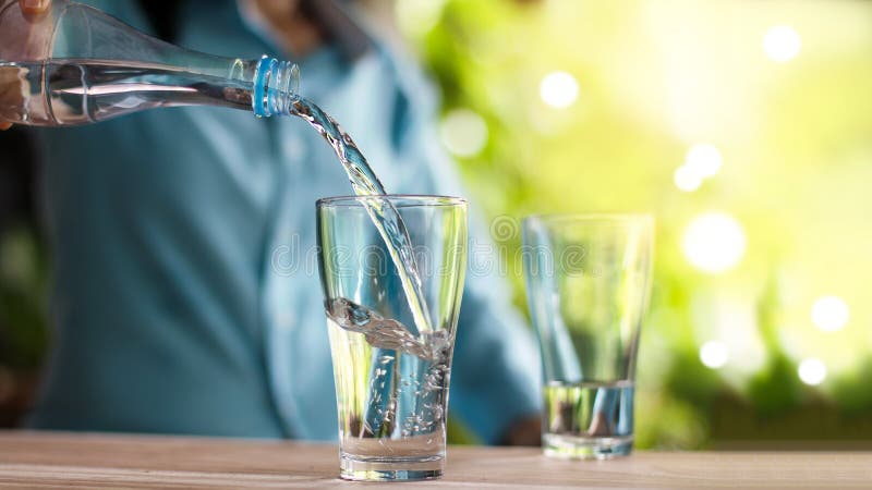 Woman`s hand pouring drinking water from bottle into glass