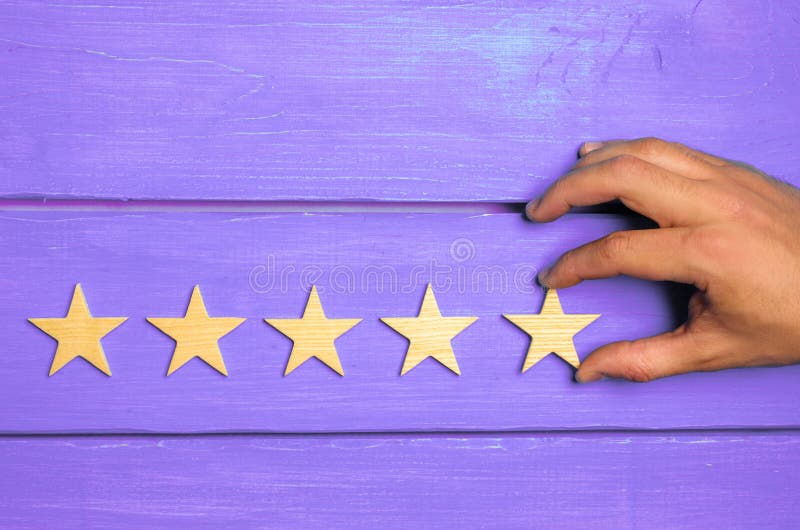 A woman`s hand puts the fifth star. Quality status is five stars. A new star, achievement, universal recognition.The critic determines the rating of the restaurant, hotel, institution. Quality mark