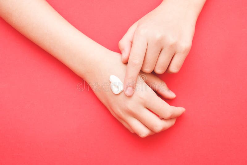 The woman`s hand smeared her hand with cosmetic cream lotion with a copy of space on a red background of minimalism. The concept