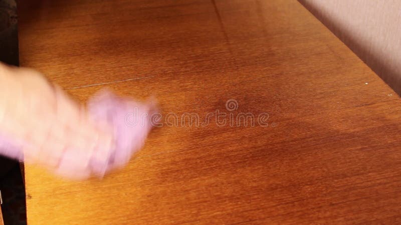 A woman`s hand wipes the dust from an old polished table.