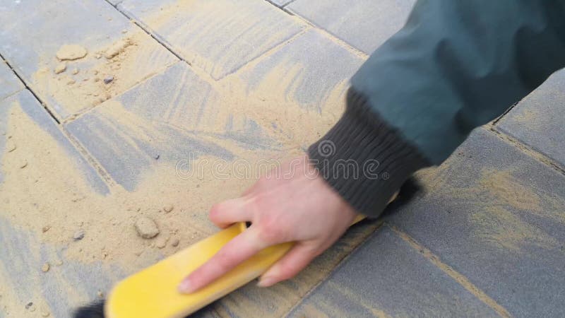 Woman`s hand wipes seams between new paving tiles with a brush-whisk - 11s