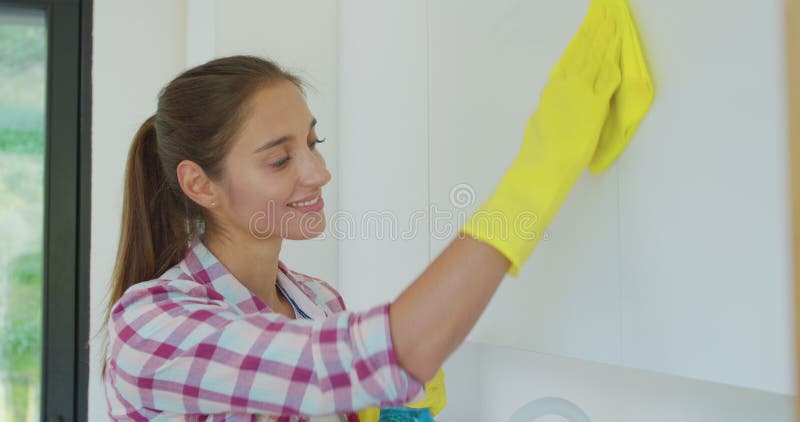 Woman`s hand in a yellow rubber glove cleans the shiny surface of a modern plastic kitchen Cabinet with a cloth. The stock image Woman`s hand in a yellow rubber glove cleans the shiny surface of a modern plastic kitchen Cabinet with a cloth. The stock image