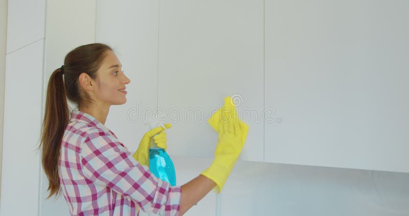 Woman`s hand in a yellow rubber glove cleans the shiny surface of a modern plastic kitchen Cabinet with a cloth. The stock photo Woman`s hand in a yellow rubber glove cleans the shiny surface of a modern plastic kitchen Cabinet with a cloth. The stock photo