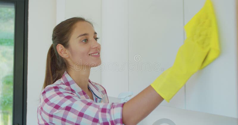 Woman`s hand in a yellow rubber glove cleans the shiny surface of a modern plastic kitchen Cabinet with a cloth. The royalty free stock photo Woman`s hand in a yellow rubber glove cleans the shiny surface of a modern plastic kitchen Cabinet with a cloth. The royalty free stock photo