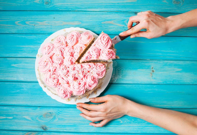 Woman`s hands cut the cake with pink cream on blue wood background. Pink cake.