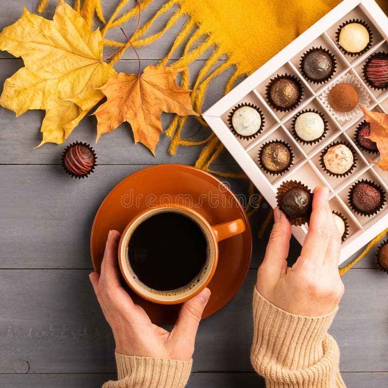 Woman`s hands holding a cup of hot black coffee orange scarf box of chocolates autumn background. Top view flat layout.