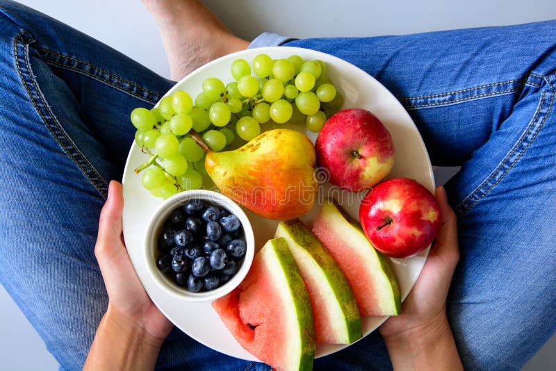 Woman`s hands holding plate with summer fruits: watermelon, blueberry,apples,pear and grape on white plate.