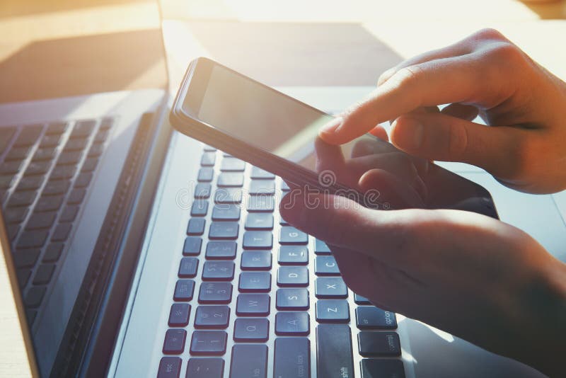 Woman`s hands holding and using smart phone, touching screen and working on laptop, stock photo Woman`s hands holding and using smart phone, touching screen and working on laptop, stock photo