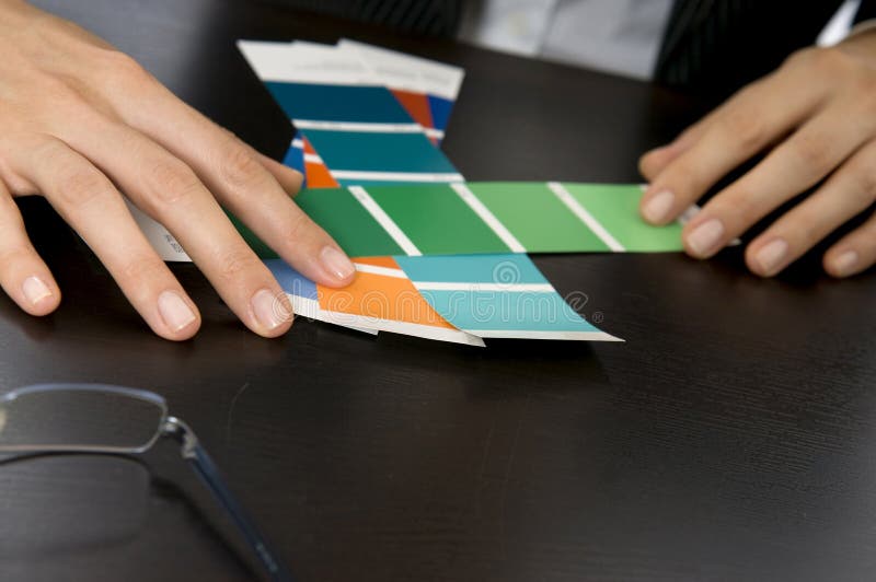 A close up of a woman's hands looking through swatches. Her eye glasses are off to the side and in the background you can see her blurred business suit. A close up of a woman's hands looking through swatches. Her eye glasses are off to the side and in the background you can see her blurred business suit.