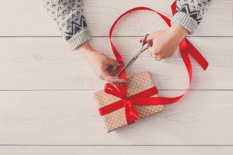 Woman`s hands wrapping christmas holiday present with red ribbon