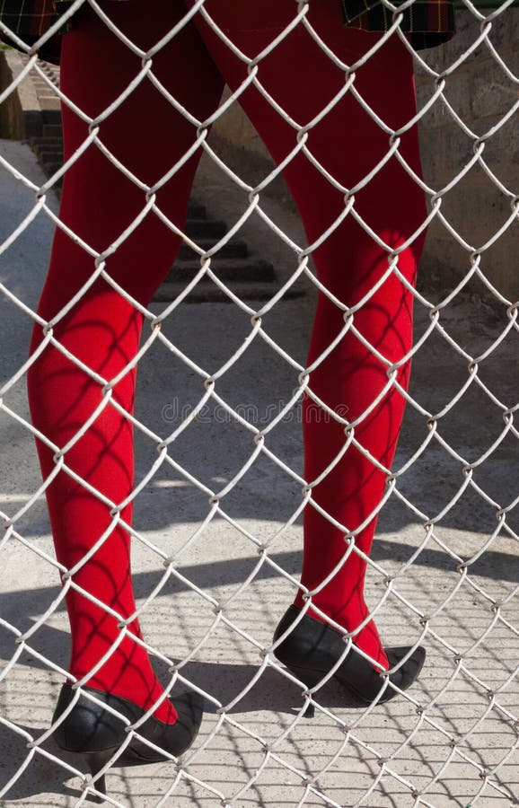 Woman`s legs in red tights behind the metal mesh fence