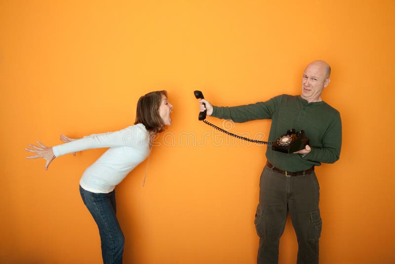 Middle-aged man holds telephone while woman screams at it. Middle-aged man holds telephone while woman screams at it
