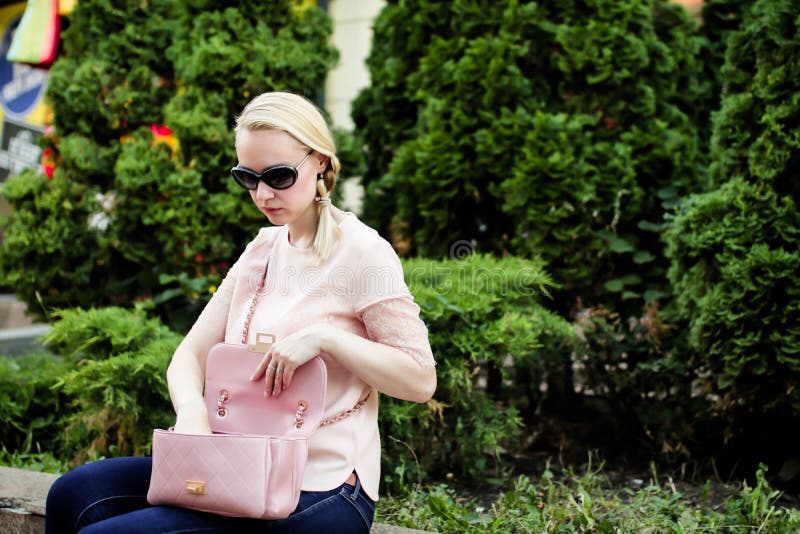 Young blond woman searching for stuff in her handbag