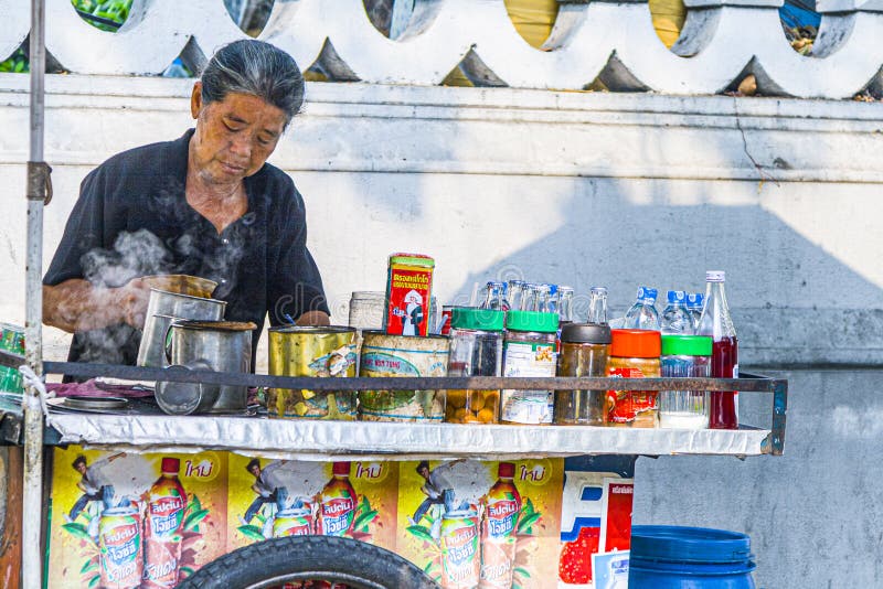 woman sells tea and food at the street in Bangkok. Most people in Thailand eat at these cheep foodstalls