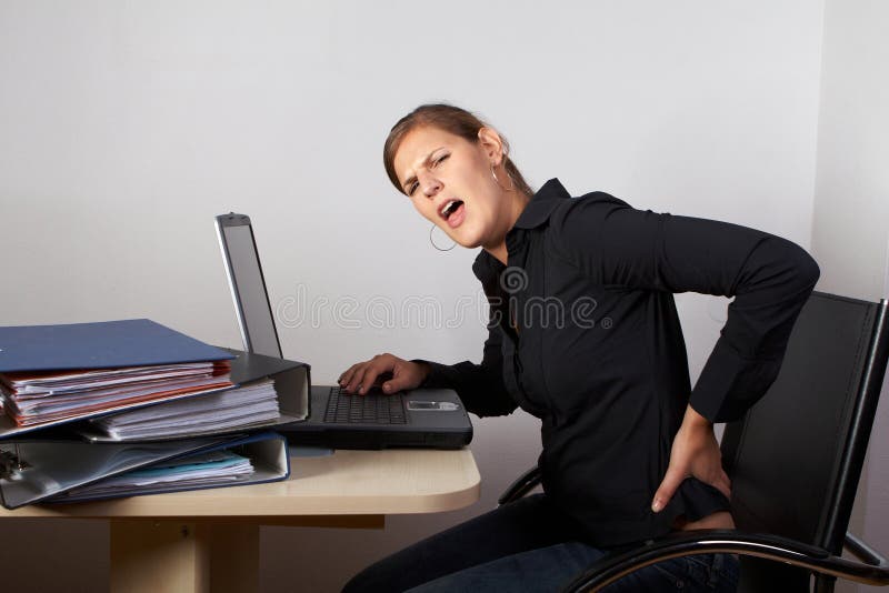 Young woman sitting at her laptop with a lot of work in front of her. She has a pain in her neck / back. Young woman sitting at her laptop with a lot of work in front of her. She has a pain in her neck / back.