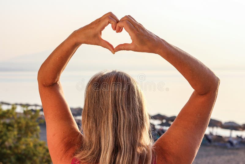 Woman Showing Heart With Her Fingers and Facing the Sea Early in