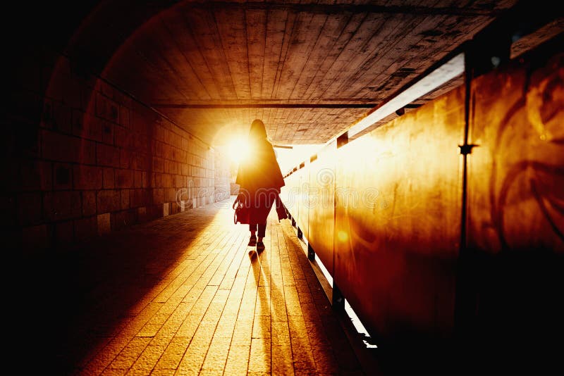 Rear view of woman silhouette in tunnel with sunset sun rays, Woman walking lonely at city street. Rear view of woman silhouette in tunnel with sunset sun rays, Woman walking lonely at city street