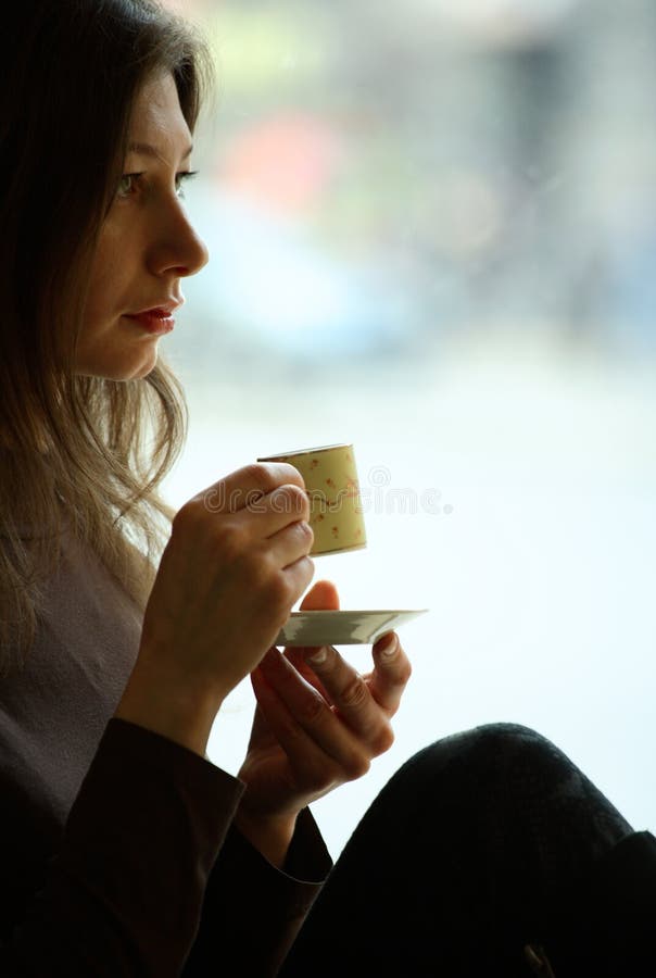 Woman sit near the window and drink coffee