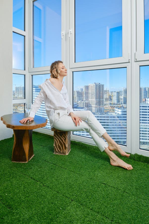 Woman sits on the balcony of her new apartment and admires the view of the city from the window