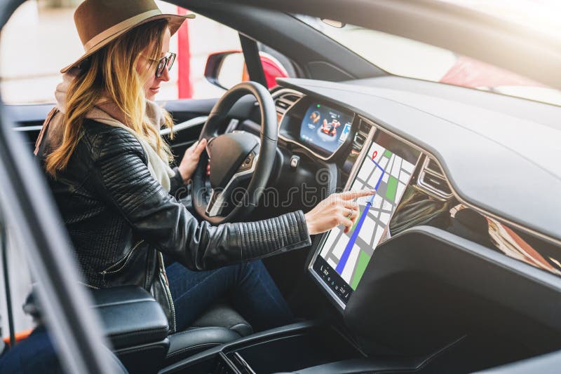 Woman sits behind wheel in car and uses electronic dashboard. Girl traveler looking for way through navigation system.