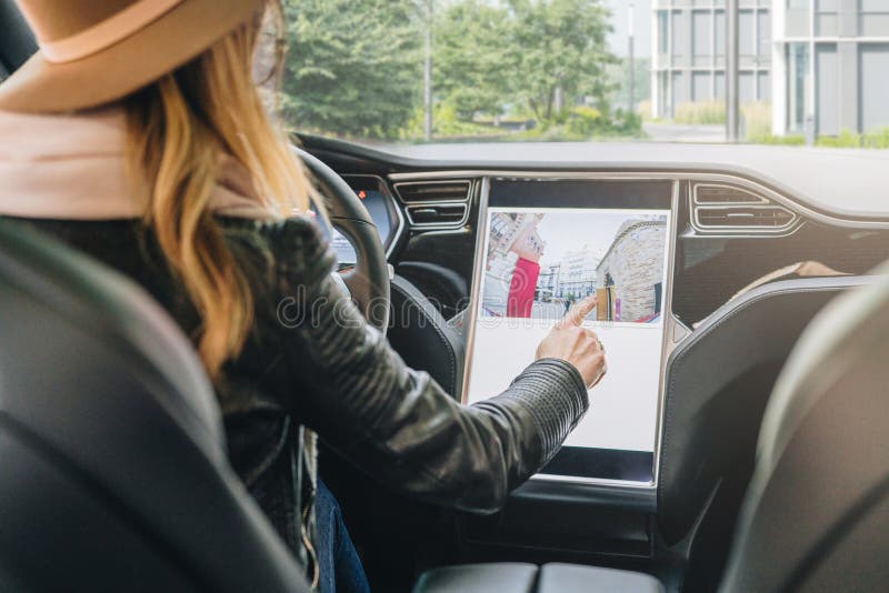 Woman sits behind wheel in car and uses electronic dashboard. Girl traveler looking for way through navigation system.