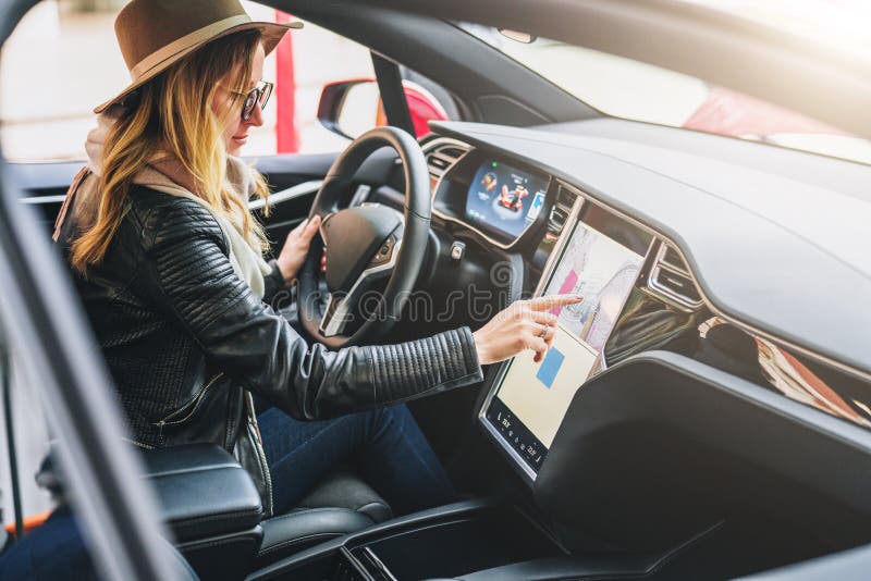 Woman sits behind wheel in car and uses electronic dashboard. Girl traveler looking for way through navigation system.