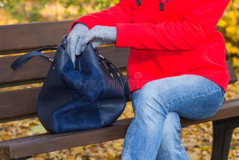 Woman sitting on bench in autumnal park and opening her handbag