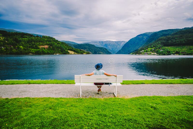 Woman sitting on a bench looking at the fjord in Ulvik, Norway. Fjord coastal promenade in Ulvik, Hordaland county, Norge. Lonely