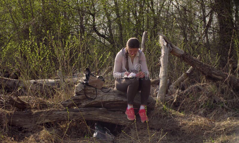 Woman sitting on a big fallen tree and writing in a diary