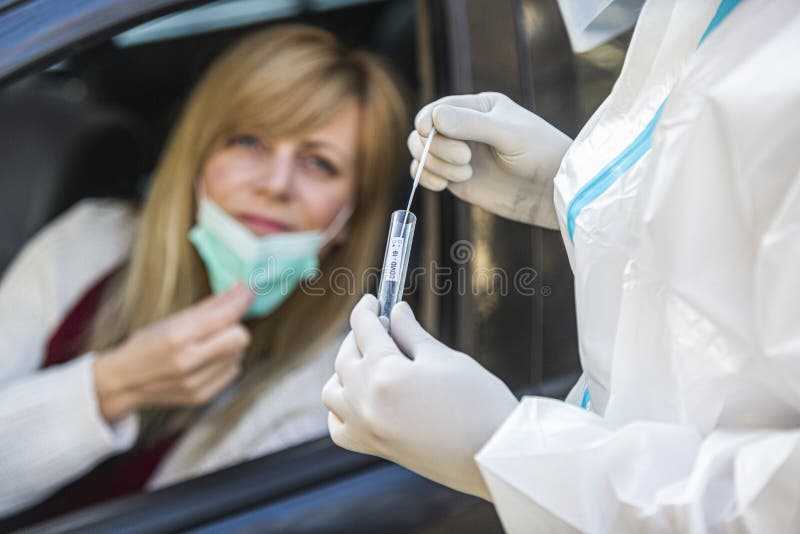 Woman sitting in car, waiting for medical worker in PPE to perform drive-thru COVID-19 test