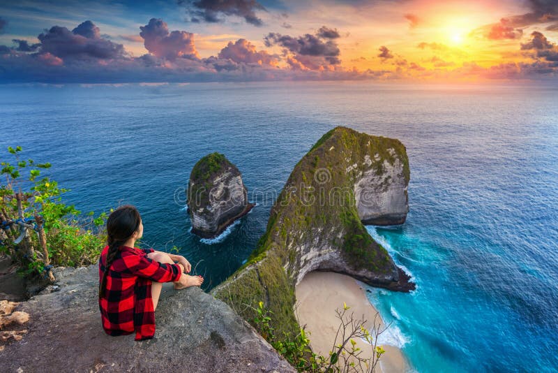 Woman sitting on cliff and looking at sunset at Kelingking Beach in Nusa penida island, Bali, Indonesia.