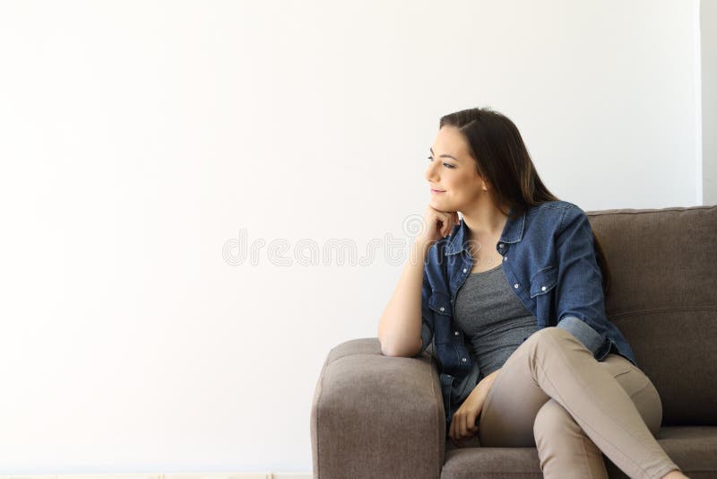 Satisfied woman sitting on a couch looking at a white isolated wall at side...