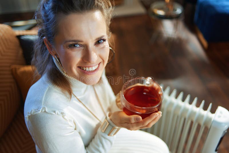 Woman Sitting on Couch Near Oil Radiator and Holding Tea Cup Stock ...