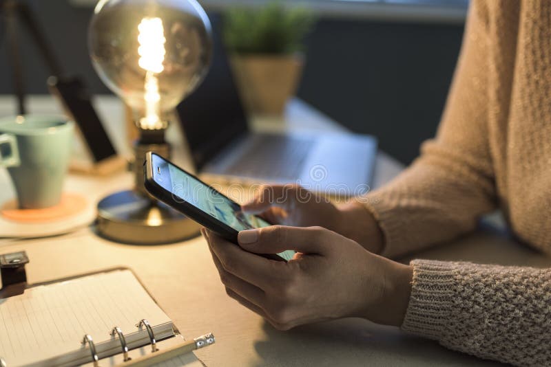 Woman sitting at desk and connecting with her phone stock photos