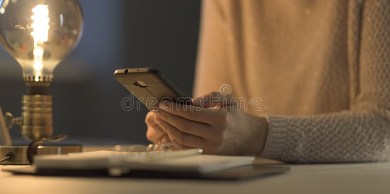 Woman sitting at desk and connecting with her phone royalty free stock images