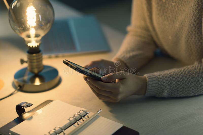 Woman sitting at desk and connecting with her phone stock photos