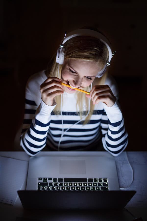 Woman sitting at desk, working on laptop at night.