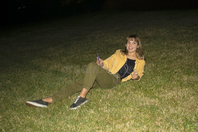 Woman sitting on grass in a park at night using mobile phone stock photo