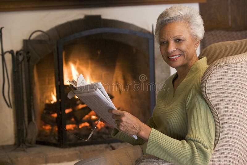 Woman sitting in living room by fireplace with newspaper