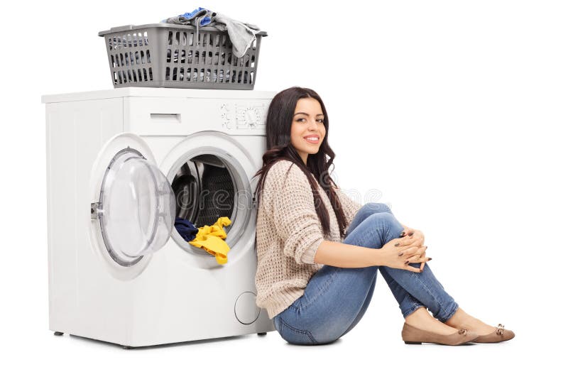 Cheerful young woman sitting on the floor next to a washing machine isolate...